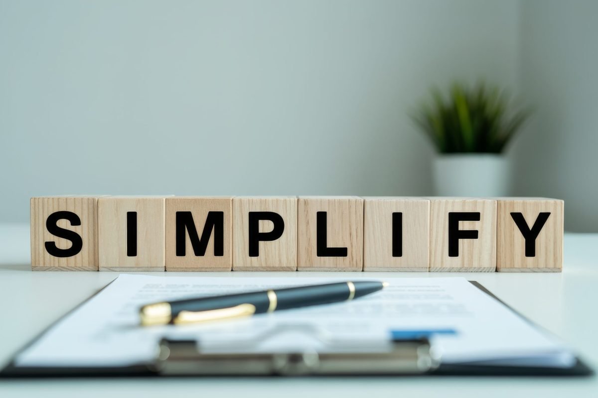 A clean workspace featuring wooden blocks spelling "SIMPLIFY" alongside a pen and a clipboard, emphasizing organization and clarity.